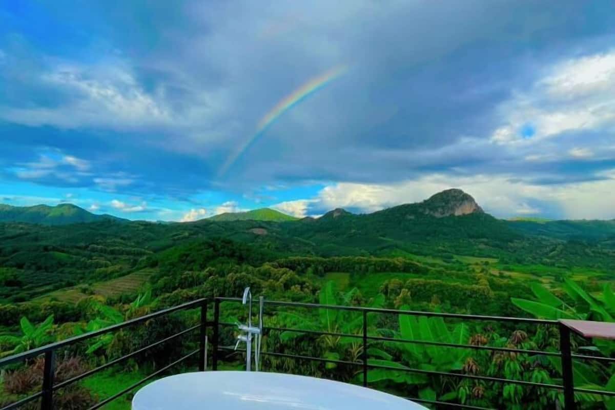 A panoramic view of lush green hills and a mountain with a rainbow in the sky.