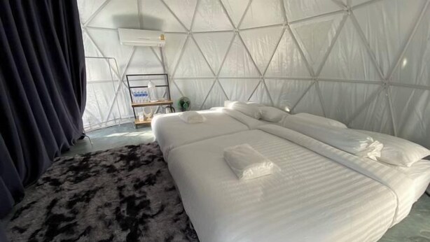 A room with a bed, a rug, a small table with a lamp, and a wall-mounted air conditioner. - Sky Bay Chiangkhan (Chiang Khan)