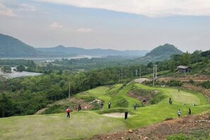 A golf course with multiple players, a water body in the background, and hilly terrain. - Sky Bay Chiangkhan (Chiang Khan)