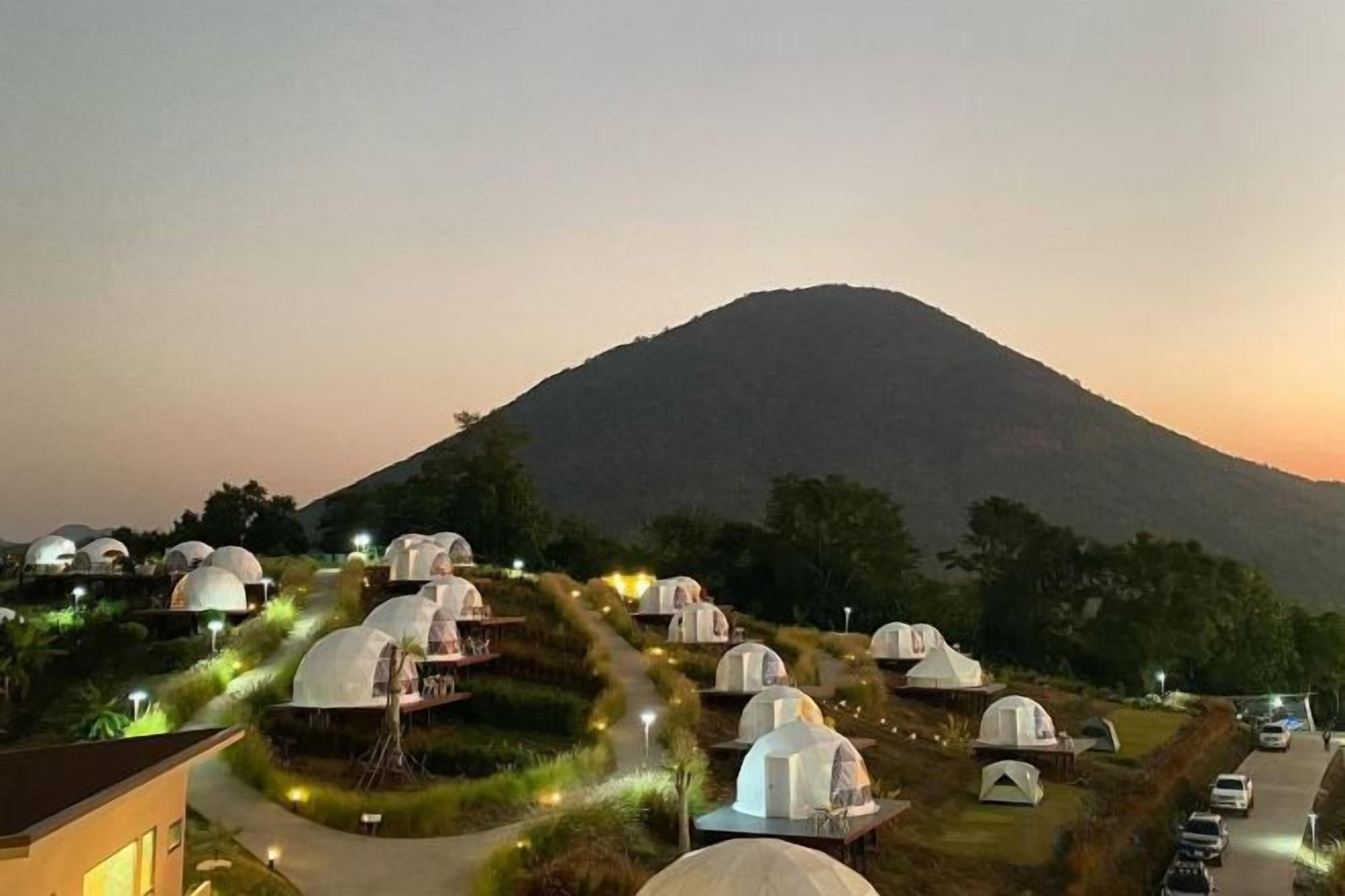 Dome-shaped accommodations with pathways, set against a backdrop of a mountain and a clear sky.