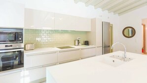 A modern kitchen with white cabinetry, a stainless steel refrigerator, a microwave, and a built-in oven. - Villa Jupeter (Corfu)