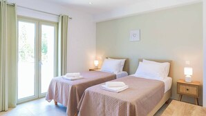 A hotel room with two beds, a sliding glass door, and a small bedside table with a lamp. - Villa Jupeter (Corfu)