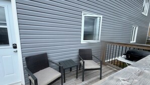 A covered porch with two chairs and a small table, a grill, and a door with a keypad lock.