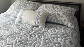A neatly made bed with patterned bedding and a pillow, a framed picture on the wall, and a textured ceiling.