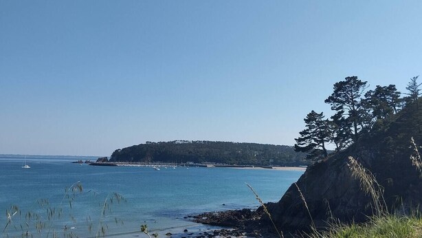 A coastal landscape with a sandy beach, grassy foreground, and a forested island in the distance.