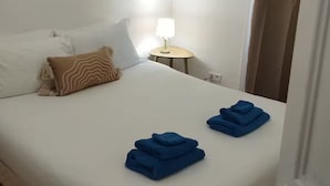 A neatly made bed with white and brown pillows, a small bedside table with a lamp, and two folded blue towels.
