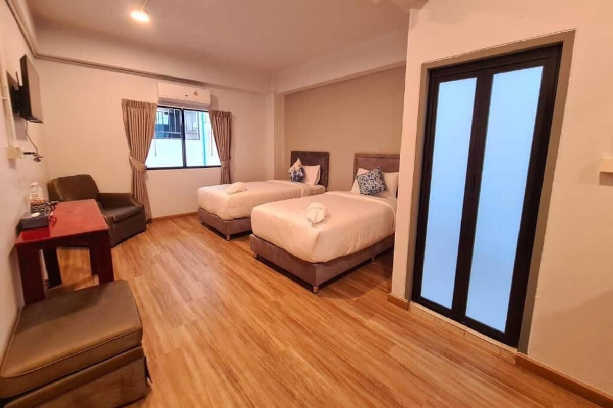 Une chambre d’hôtel avec deux lits, un bureau, une chaise et une fenêtre avec des rideaux.