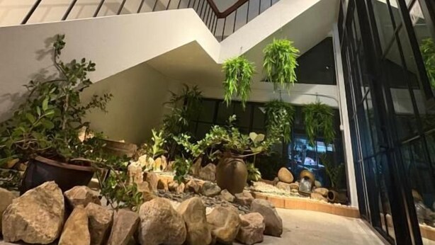 Un intérieur à plusieurs niveaux, agrémenté d’un jardin de rocaille central et de plantes suspendues, avec un escalier moderne et des rampes en verre.