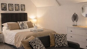 Un dormitorio con una cama, un sofá gris, un aparador blanco y un espejo.