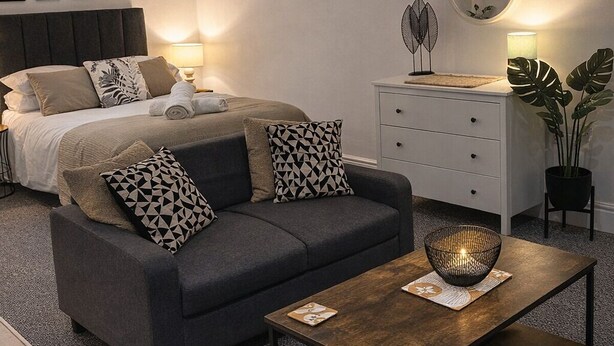 Un dormitorio moderno con cama, sofá gris y una mesa de centro de madera.