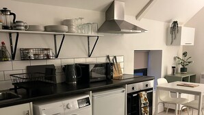 Cocina compacta con lavadora, microondas y tostadora. Hay un comedor con mesa y sillas.