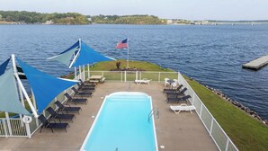 Ett poolområde med solstolar och parasoller, en flagga och utsikt över vattnet.
