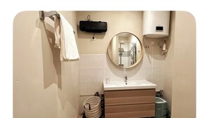 Een badkamer met een witte wastafel, een ronde spiegel, een handdoekhouder, een zwarte wandverwarming en een wit toilet.