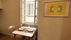 Een eethoek met een tafel gedekt voor twee personen, een raam en een kunstwerk in een lijst aan de muur.
