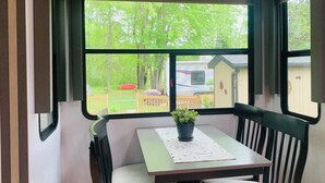 Ein kleiner Tisch mit einem Blumentopf, zwei Stühle und Blick auf einen Garten mit Bäumen und einem kleinen Gebäude.