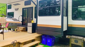 Ein Wohnmobil mit überdachter Außenterrasse, Picknicktischen und Recyclingbehältern.