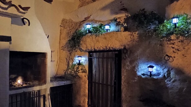 A rustic stone building with a fireplace, a wooden door, and multiple small windows with lights.