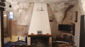 A rustic room with a fireplace, two rocking chairs, a brick wall, and a television mounted on the wall.