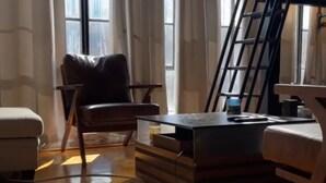 A living room with a wooden floor, a black leather chair, a small table, and a ladder.