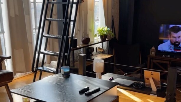 A cozy living room with a wooden coffee table, a ladder, a television, and a plant.