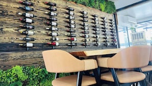 Un porte-bouteilles fixé au mur, avec différentes bouteilles, un panneau en bois et un coin salon avec des chaises.