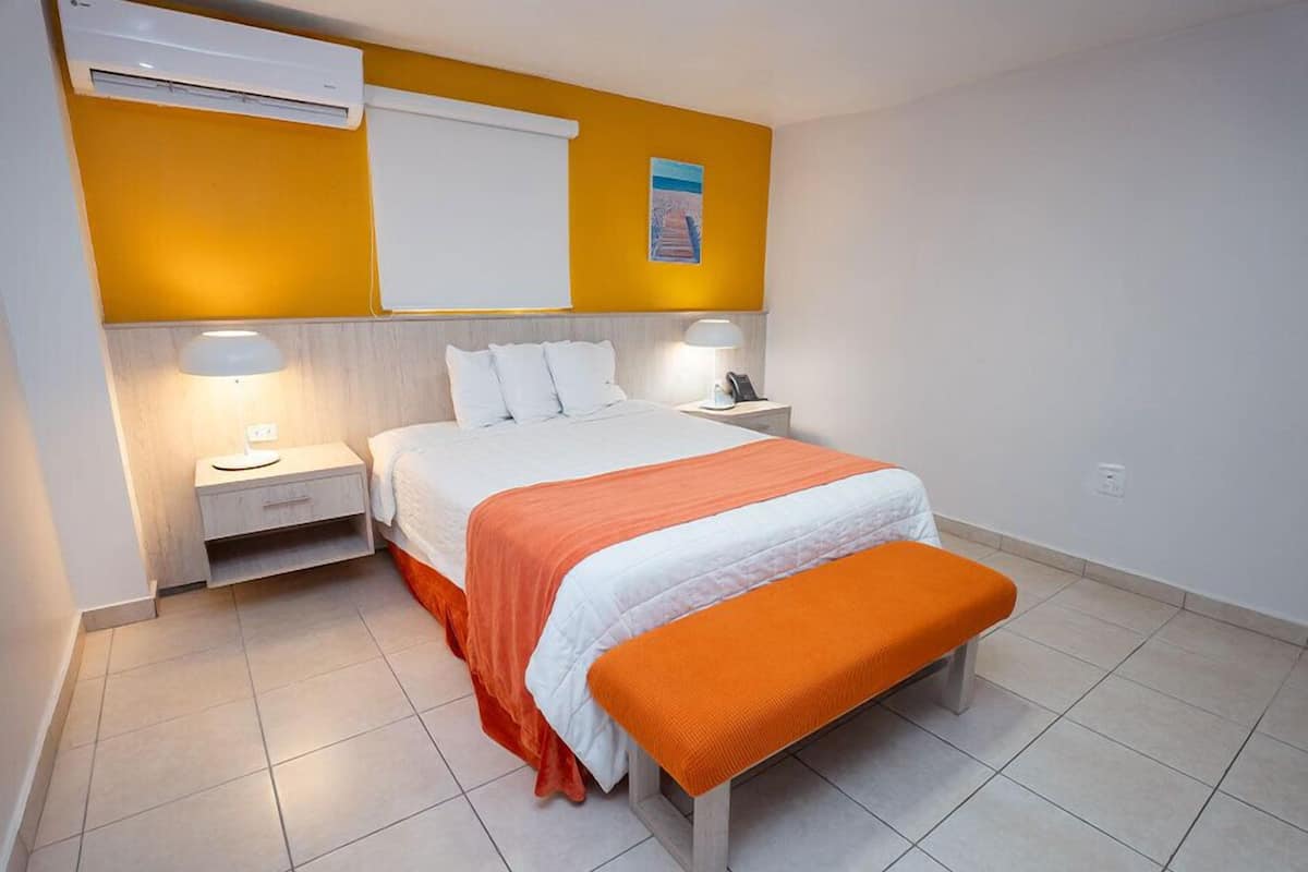 A hotel room with a bed, nightstands, and an air conditioning unit.