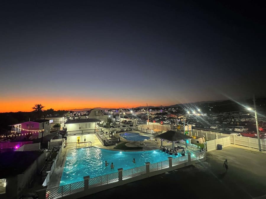 A nighttime view of a resort with a swimming pool, multiple buildings, and a parking area.