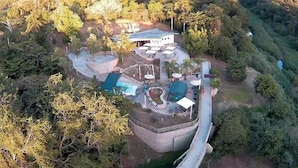 Vue aérienne d’un complexe hôtelier doté d’une piscine, d’un espace couvert et d’un bâtiment à toit en pente.