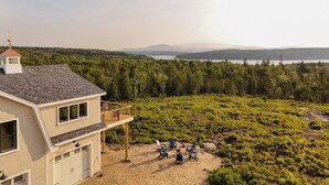 Una casa de dos pisos con garaje, balcón y vistas a un bosque y un lago.