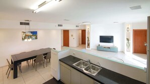 A modern kitchen with a glass partition, a dining area with a table and chairs, a TV, and a wooden door. - Washington XII - Three Bedroom Apartment, Sleeps 7 (Jerusalem)