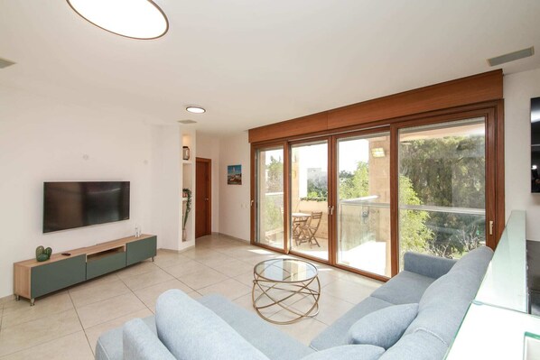Uma sala de estar moderna com televisão de tela plana, um sofá, uma mesa de centro e uma porta de vidro deslizante que dá para uma área externa.