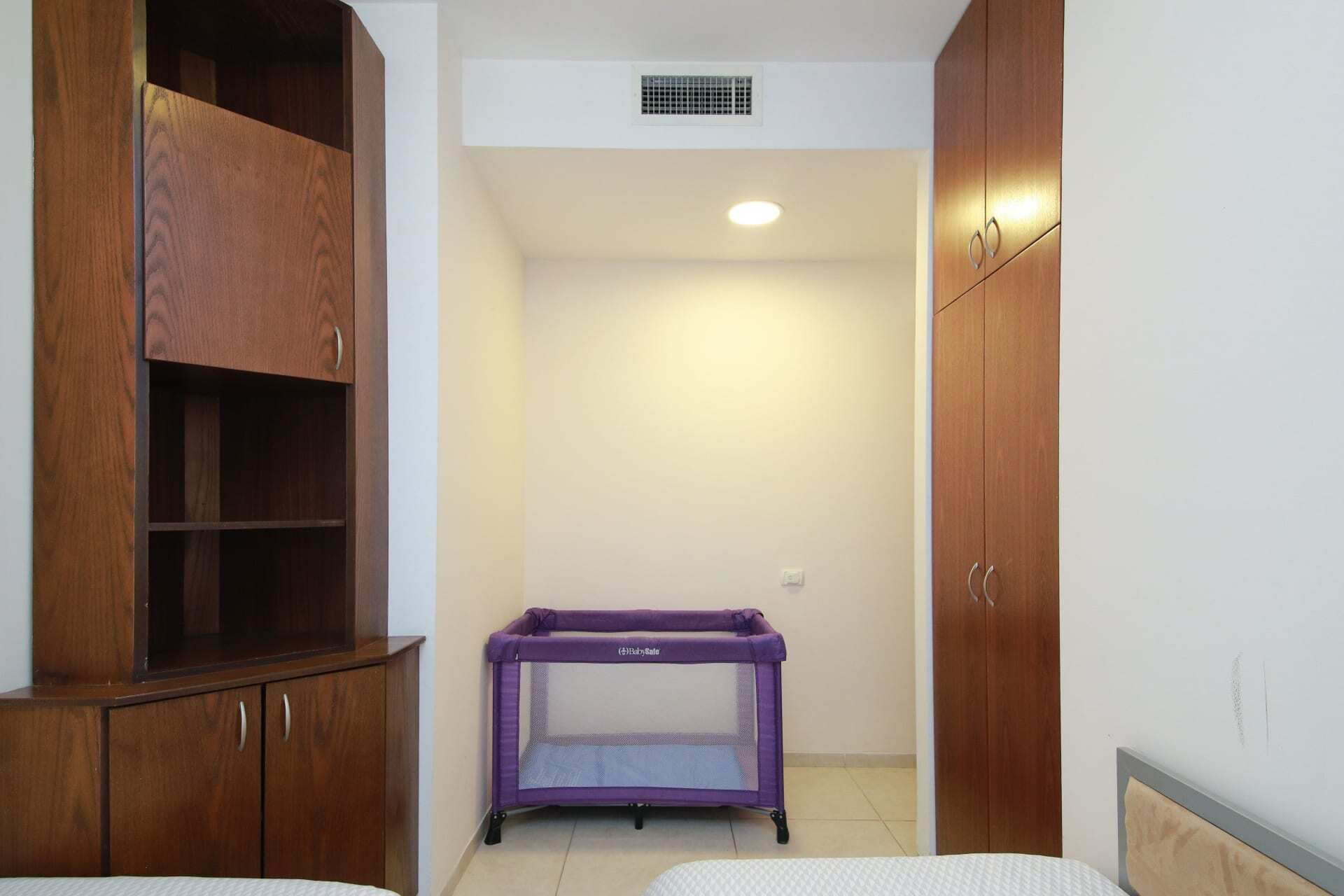 Een slaapkamer met een houten garderobe, een paars babyren en een bed.