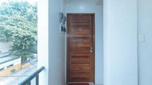 Un couloir avec une porte en bois, une moquette rouge et une vue sur un arbre et des bâtiments à l’extérieur.