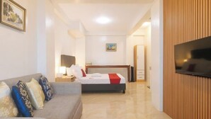 Une chambre d’hôtel avec un lit, un canapé, une télévision et un mur recouvert de panneaux de bois.