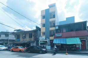 A multi-story building with a coffee shop on the ground floor, a visible storefront with a striped awning, and a parked car in front. - RedDoorz @ Delorian Residences (Makati)