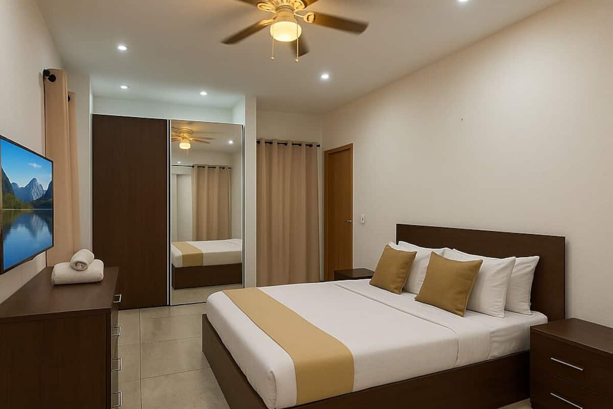 A hotel room with a bed, a TV, a ceiling fan, and a bathroom mirror.