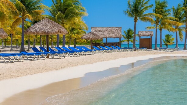 A beach with clear turquoise water, white sand, and blue lounge chairs. - Barmel Villa Rooms (Roatan)