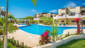 A resort with a large swimming pool surrounded by palm trees and modern buildings. - Barmel Villa Rooms (Roatan)