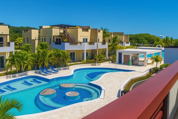 A swimming pool with lounge chairs, palm trees, and modern buildings in the background.