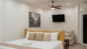 A modern hotel room with a large bed, a ceiling fan, a flat-screen TV, and a sofa. - Barmel Villa Rooms (Roatan)