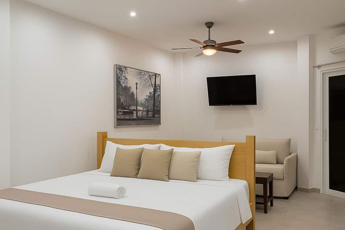 A modern hotel room with a large bed, a ceiling fan, a flat-screen TV, and a sofa.