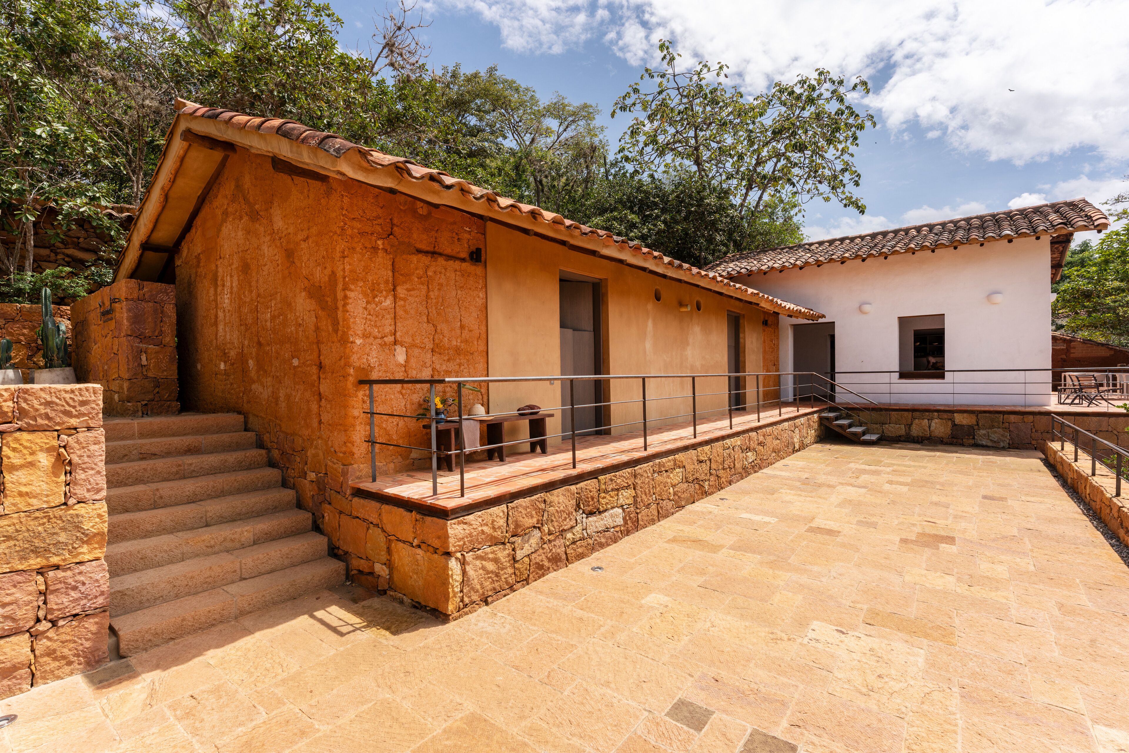 Un bâtiment rustique avec un escalier en pierre menant à une porte en bois, un petit espace extérieur aménagé avec une table et des chaises, et une terrasse carrelée.