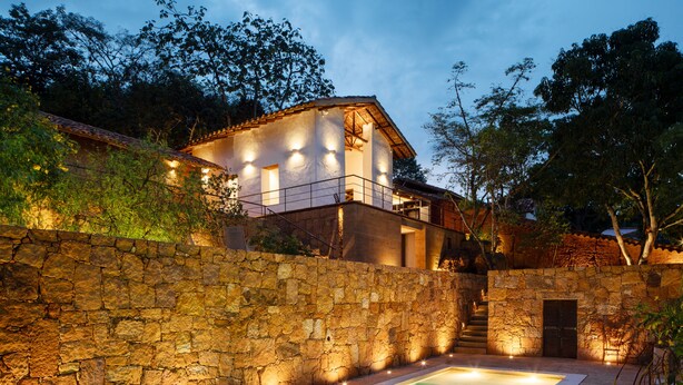Una piscina con un muro de piedra y una casa al fondo.