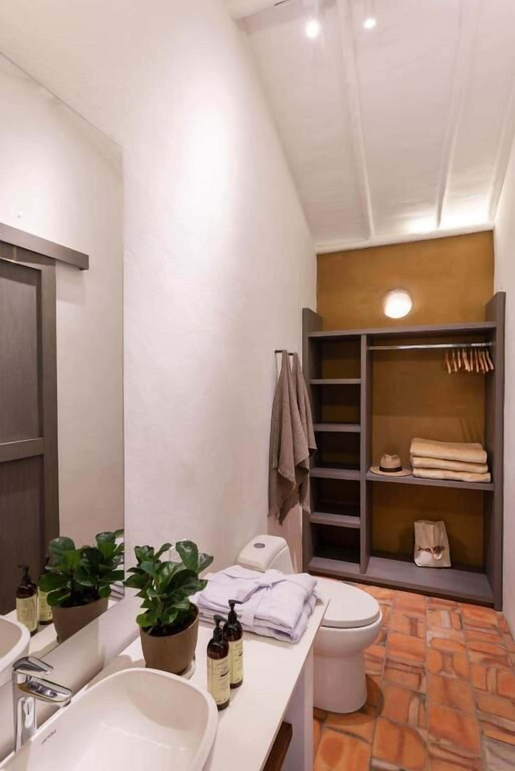 A compact bathroom with a white sink, a toilet, and a built-in shelving unit with towels and toiletries.