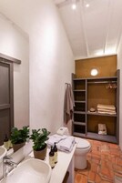 A compact bathroom with a white sink, a toilet, and a built-in shelving unit with towels and toiletries.