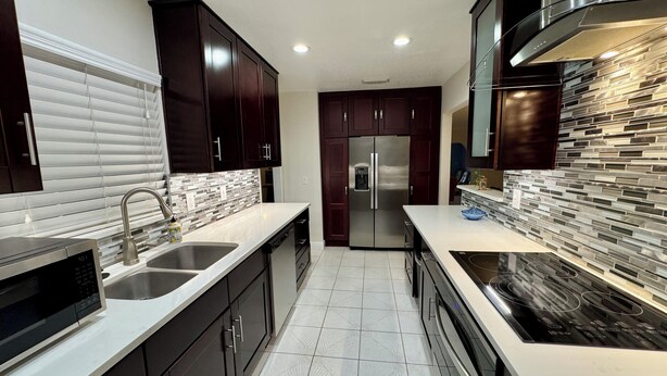A modern kitchen with dark cabinets, stainless steel appliances, and a patterned backsplash.