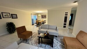 A living room with a sofa, armchairs, a coffee table, and a dining area in the background.