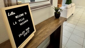 A reception desk with a welcome sign, a mirror, a lamp, framed pictures, and a potted plant.