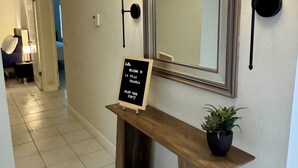 A reception area with a welcome sign, a mirror, wall-mounted lamps, and a potted plant.