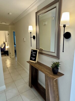 A reception area with a welcome sign, a mirror, wall-mounted lamps, and a potted plant.